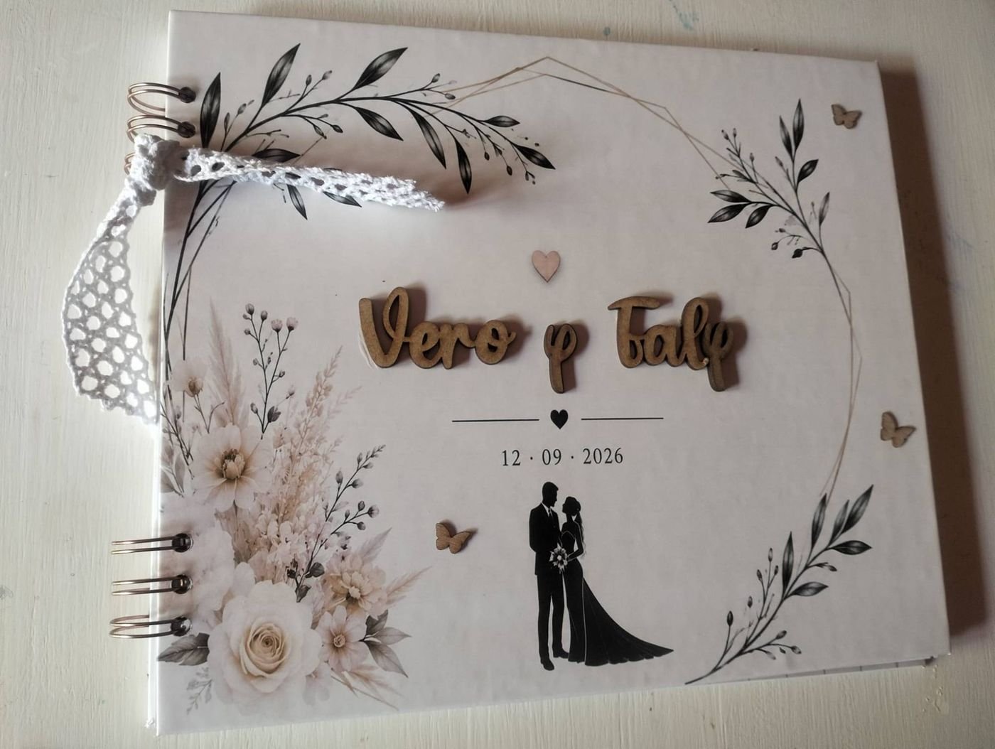 Álbum de firmas de boda con los nombres de los novios en letras de madera, mariposas de madera, ramas en blanco y negro y lazo de ganchillo