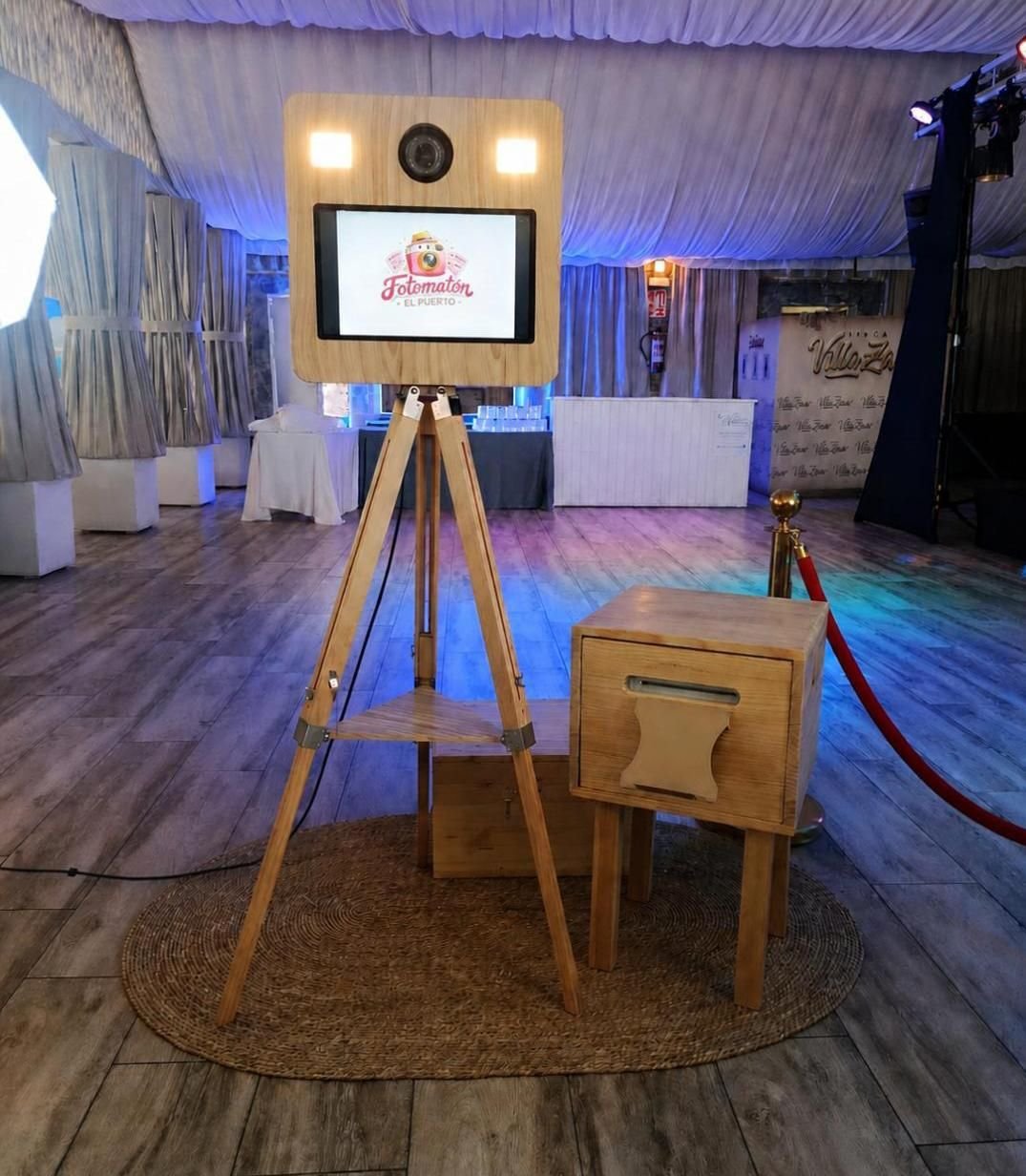 Fotomatón vintage de madera sobre trípode, con la pantalla encendida, montado en una carpa de boda